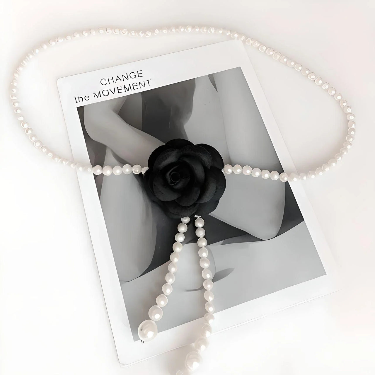 Pearl waist belt draped over a black flower on a photo with 'CHANGE THE MOVEMENT' text.