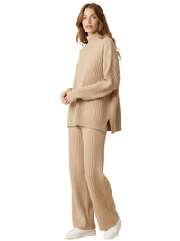 Thumbnail for Model wearing Drestiny 2-Piece Women's Knit Set in beige, featuring a ribbed turtleneck sweater and matching wide-leg pants for a minimal, elevated loungewear look — styled with white sneakers for effortless comfort.