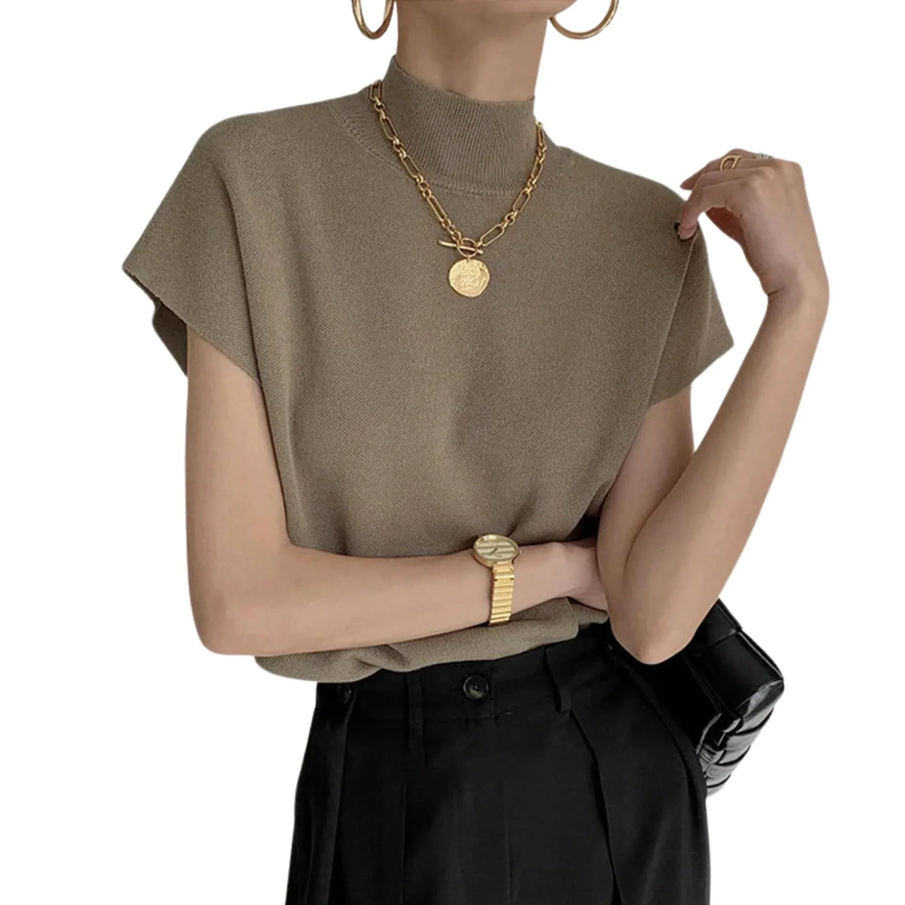 Woman wearing a khaki short sleeve sweater and black pants with gold jewelry on a white background