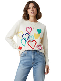 Thumbnail for Woman wearing a white sweater with colorful heart patterns and blue jeans on a white background