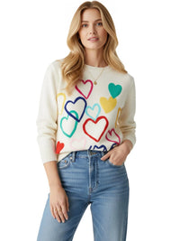 Thumbnail for Woman wearing a cream sweater with colorful heart designs and blue jeans on a white background