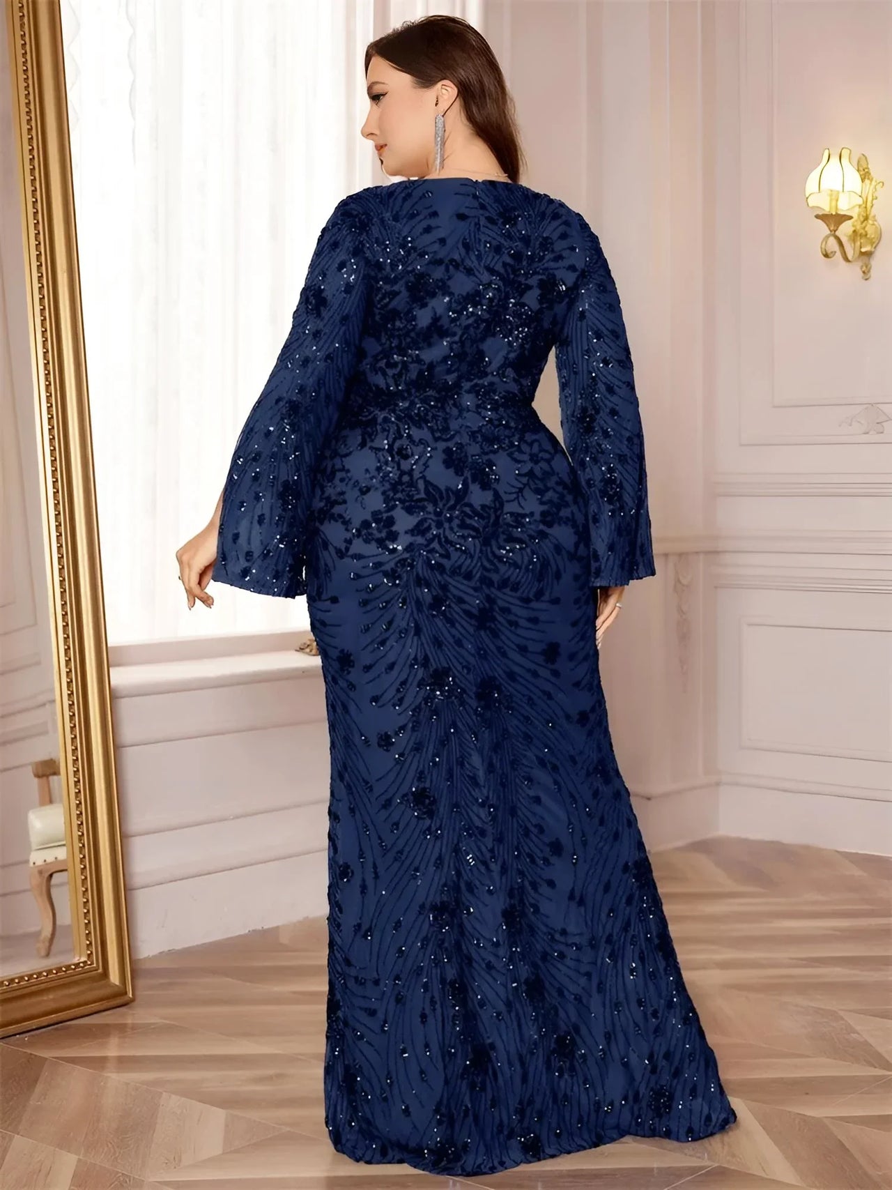 Woman wearing a navy blue sequin dress in a room with a mirror and light fixture.