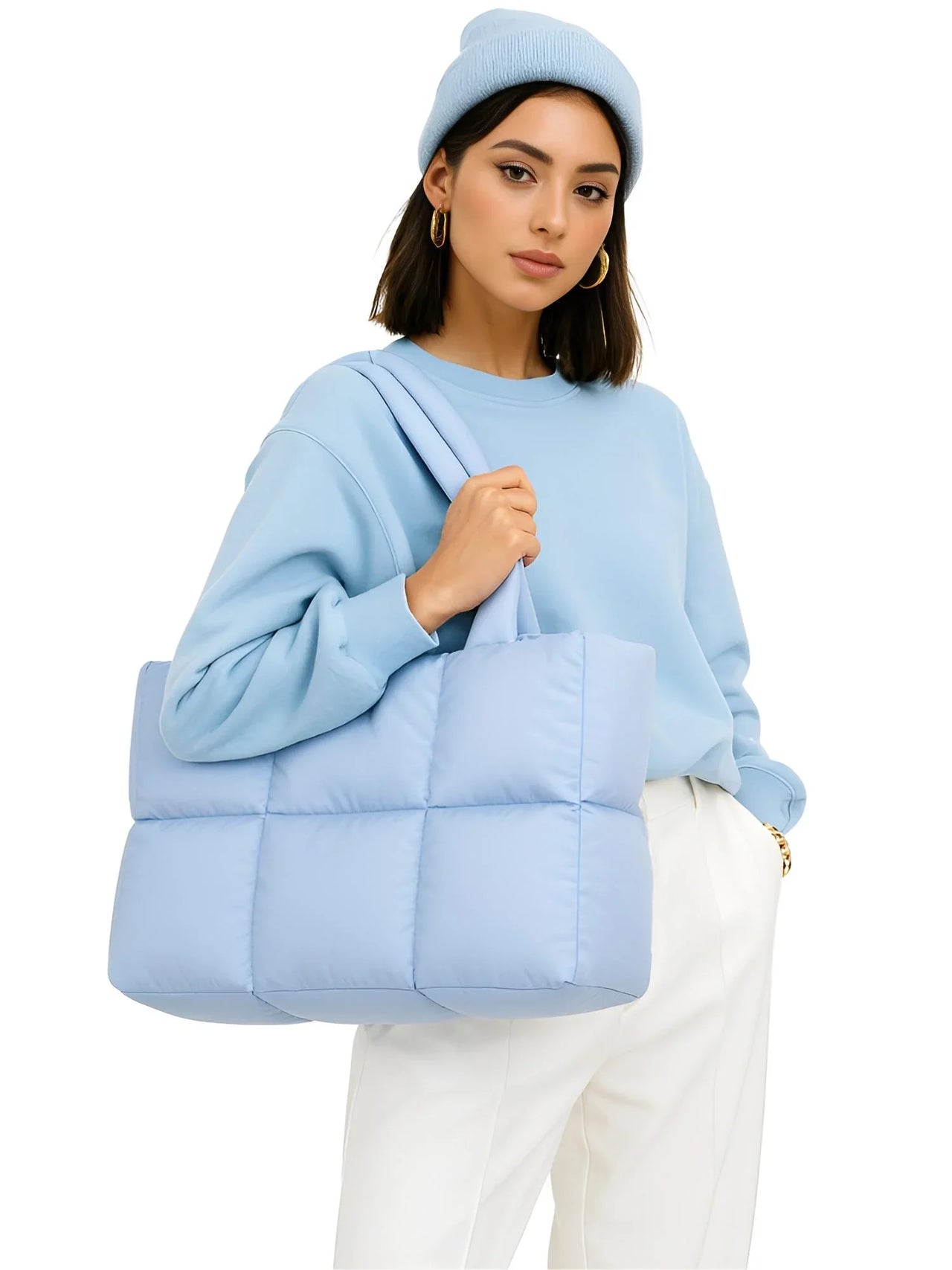 Woman wearing a light blue sweater and holding a matching light blue puffer bag against a white background