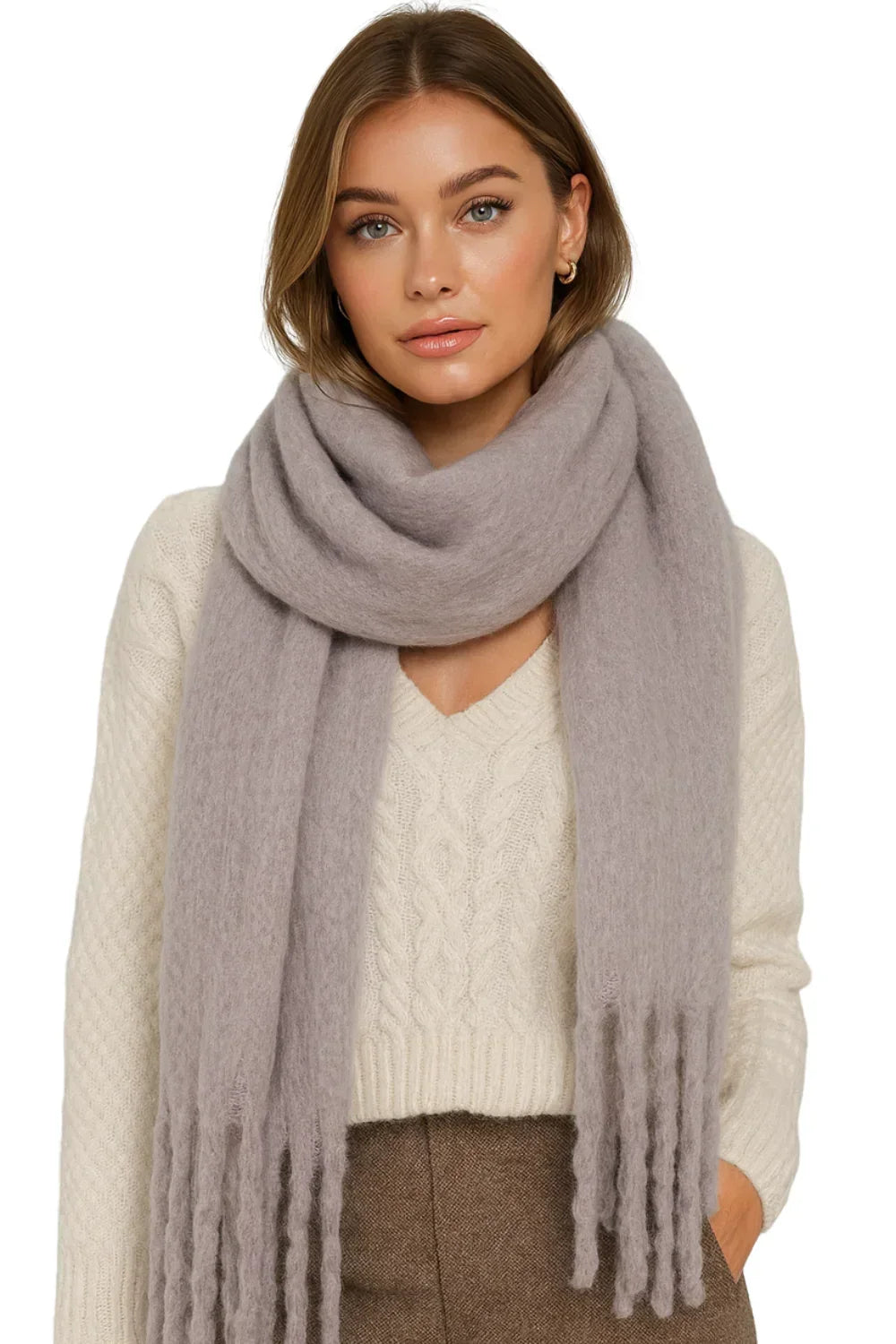 Woman wearing a large light gray blanket scarf with a white sweater and brown pants on a white background