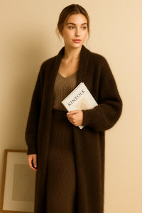 Thumbnail for Woman wearing a long fluffy brown cardigan holding a book titled 'Kinefok' against a beige wall